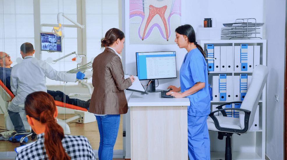 Young woman filling out dental form while sitting in a crowded waiting area with other patients talking and waiting for their appointments.