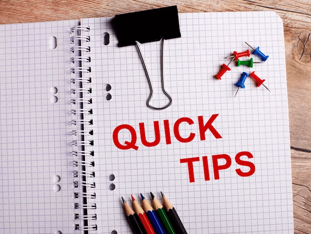 A notebook with the words 'Quick Tips' written on it, surrounded by multi-colored pencils and buttons, on a wooden surface.
