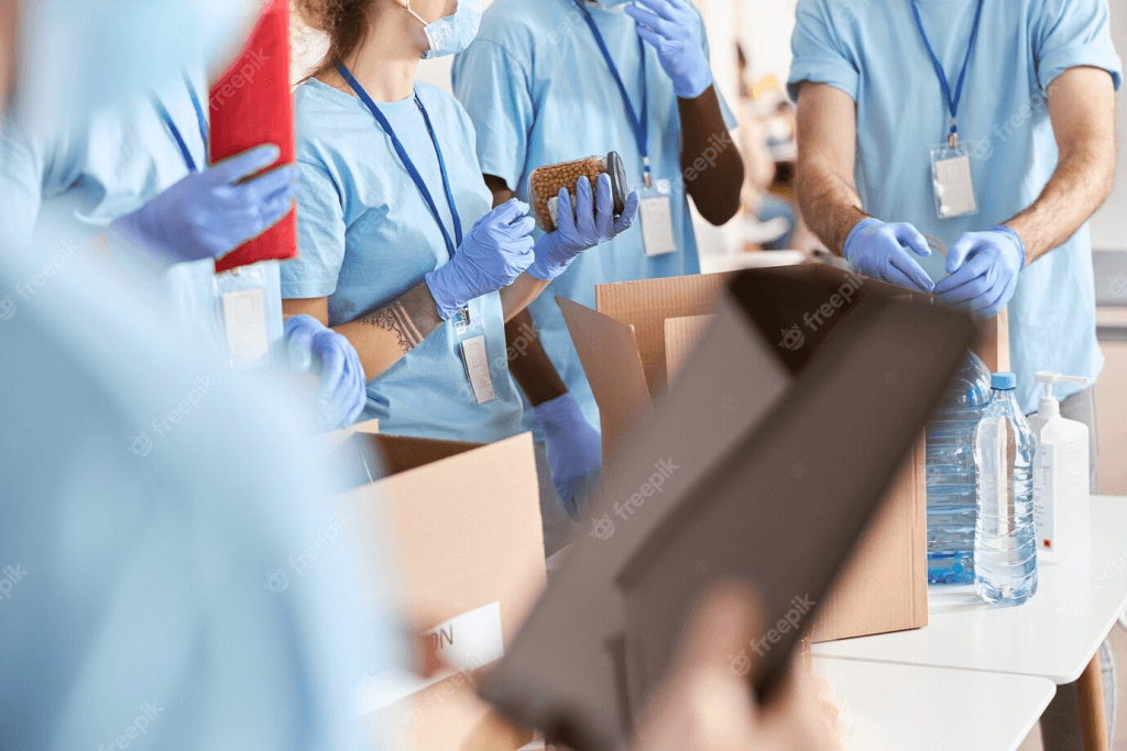 Cropped shot of volunteers in blue uniforms wearing protective masks and gloves while sorting and packing food.